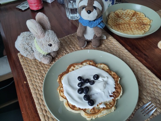 Bunbun and Sebas starring at a plate of waffles. The waffle is covered with a cream-blueberry topping.