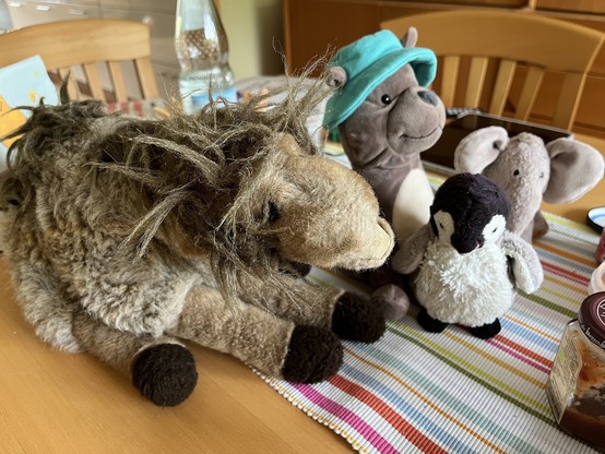 4 Plüschies auf dem Tisch: ein Kamel, ein Hund mit Hut, ein Pinguin und ein Elefant 