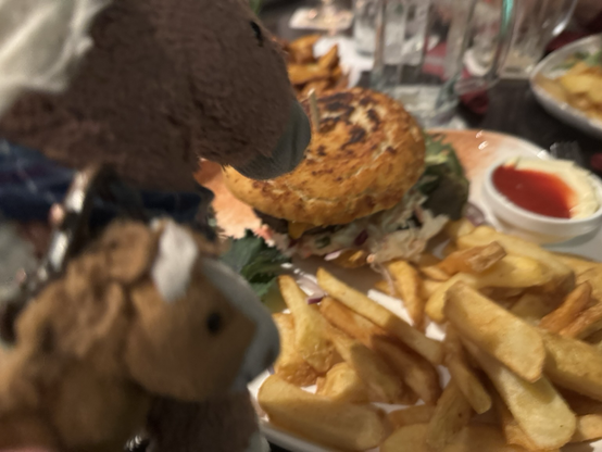 2 kleine Plüschponys vor einem Teller mit Pommes und 1 Burger. 