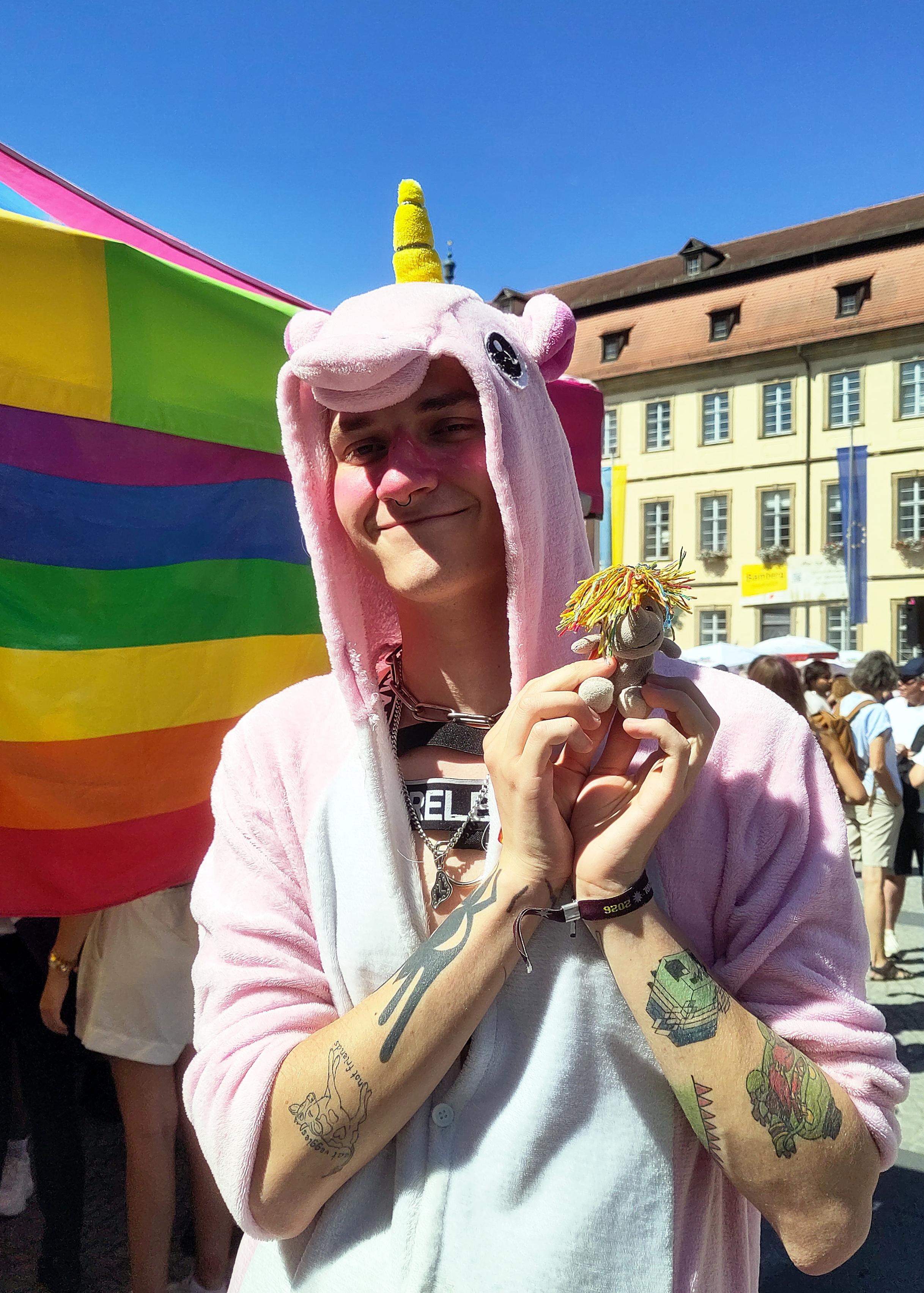 Mensch in rosa Einhorn-Onesie hält das kleine Plüscheinhorn Carola zärtlich in den Händen und schaut dabei liebevoll-verträumt.