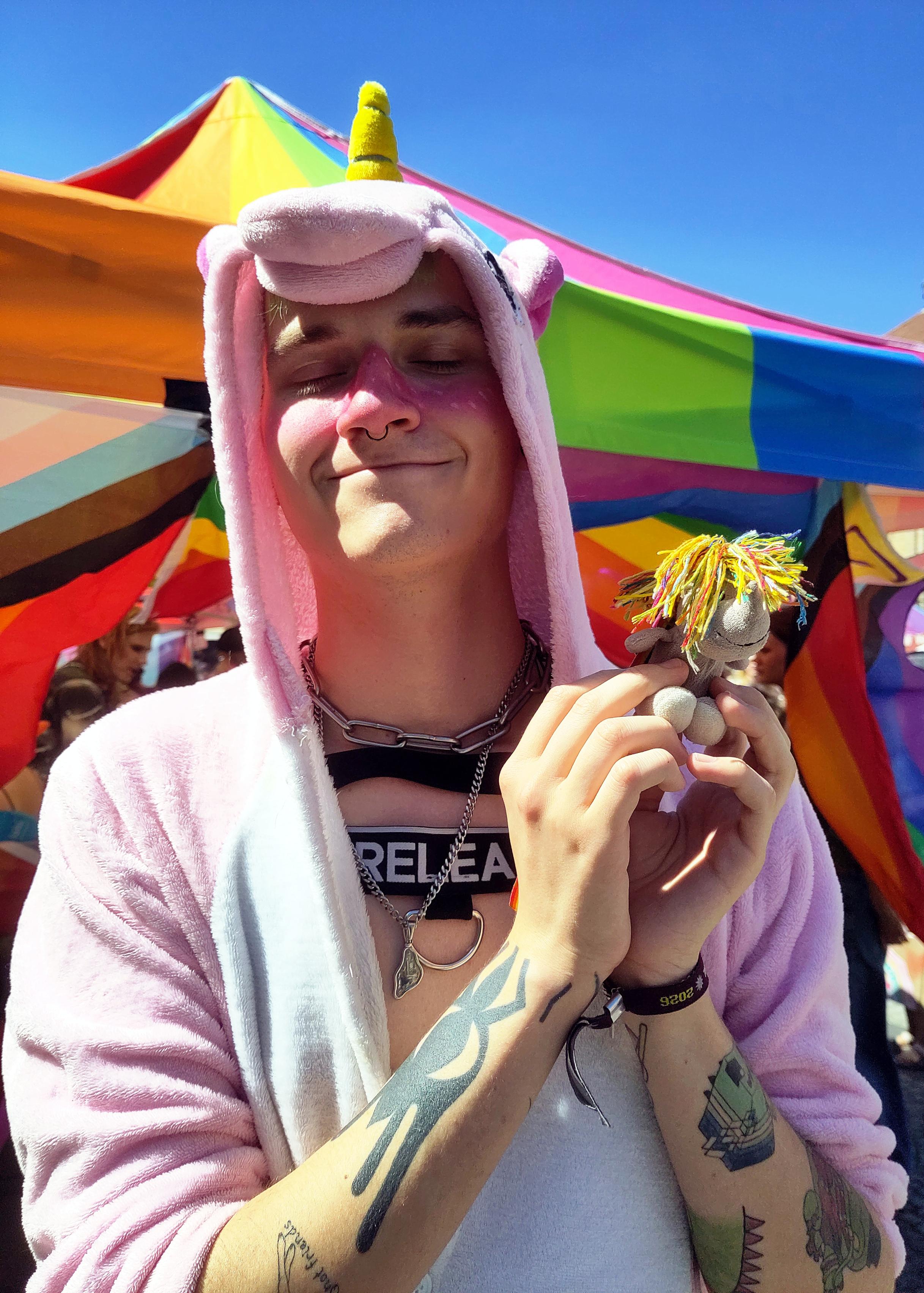 Gleiche Szene, aber etwas näher und frontaler aufgenommen:
Mensch in rosa Einhorn-Onesie hält das kleine Plüscheinhorn Carola zärtlich in den Händen und schaut dabei liebevoll-verträumt.