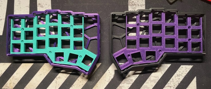 Two crkbd cases. The left is purple with a green switchplate and the right is black with a purple plate. 