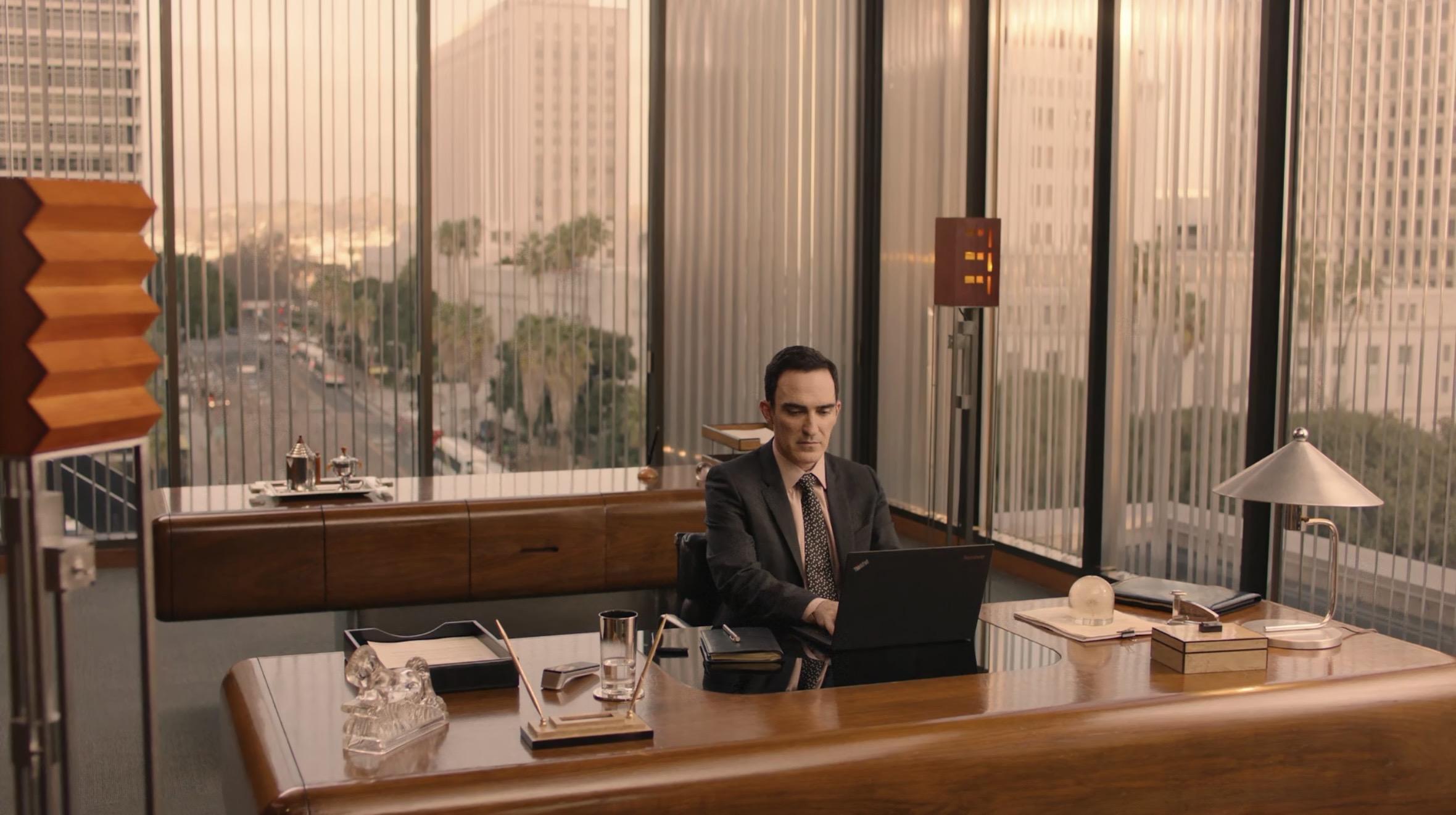 Ein orpulentes Büro mit edlen Holzmöbeln, ein Mann in Anzug benutzt ein ThinkPad