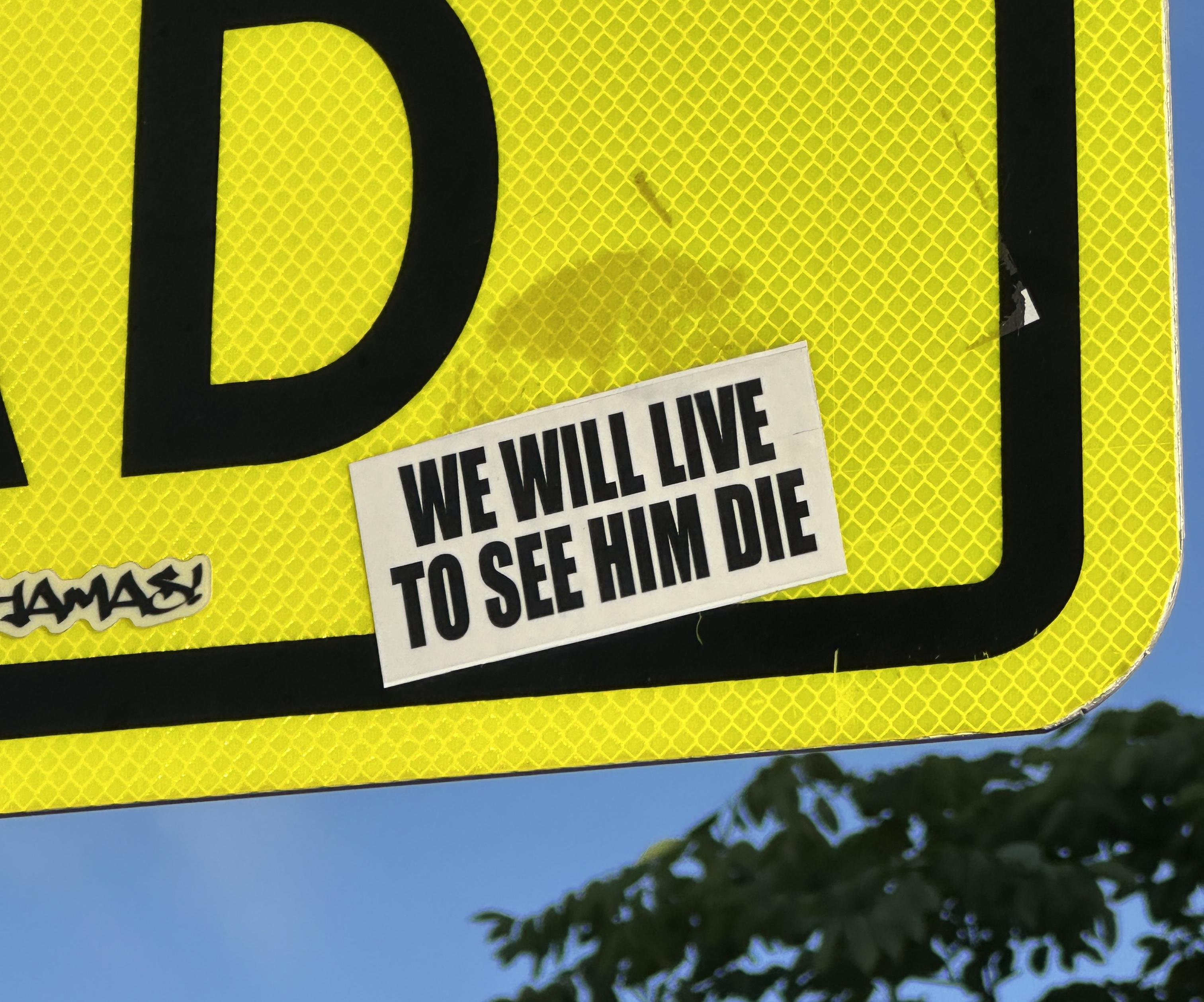 A sticker that says “we will live to see him die”