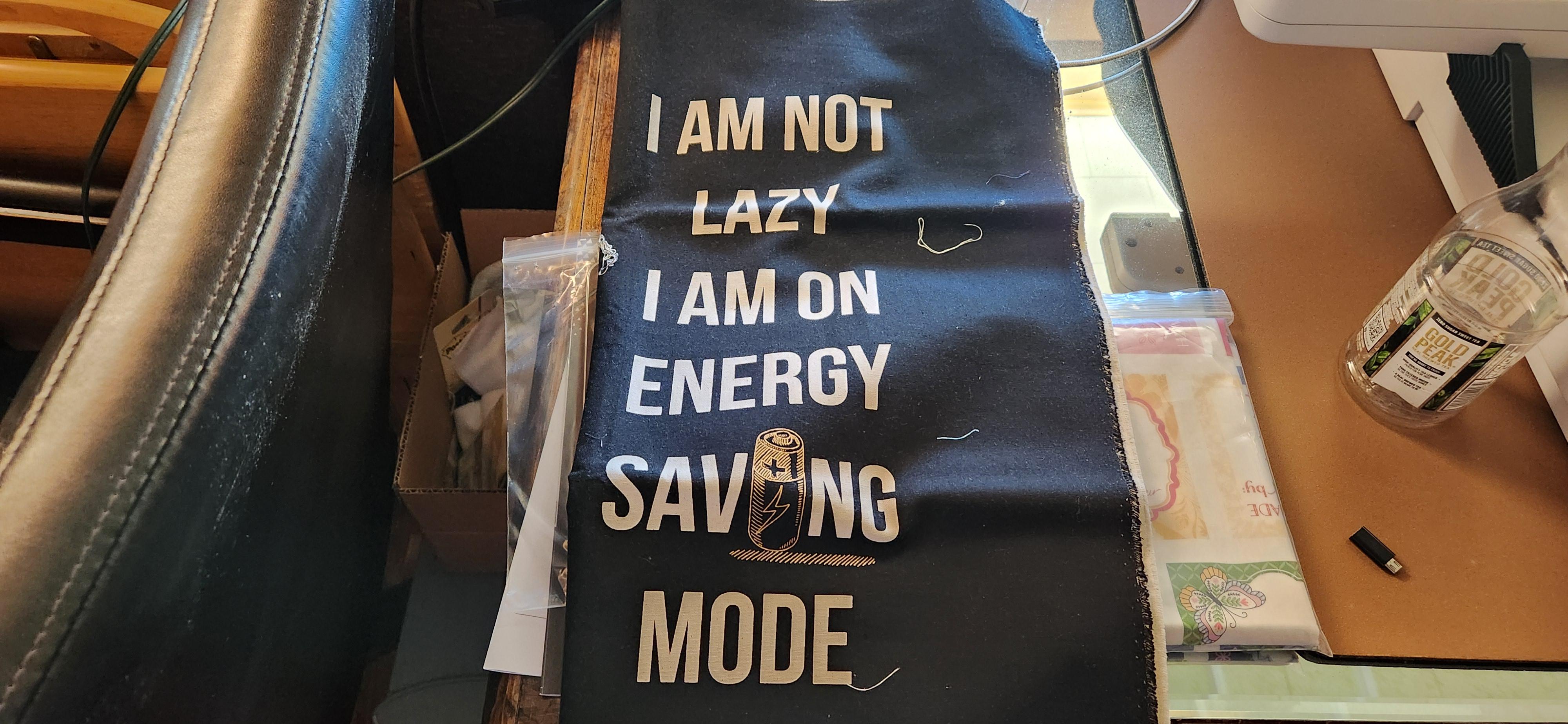 A piece of unfinished fabric sporting the bold slogan I AM NOT LAZY, I AM ON ENERGY SAVING MODE