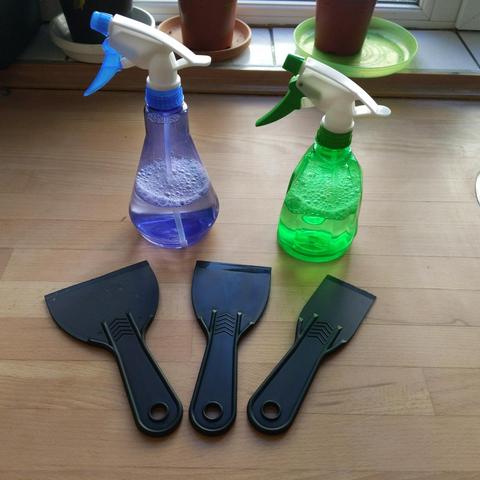 Et fotografi af 2 forstøvere med sæbevand i og 3 plastik skrabere. Det hele ligger på et køkkenbord.