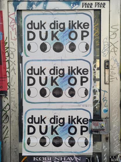 3 plakater en dør. På plakaterne står der 

Duk dig ikke 
DUK OP 