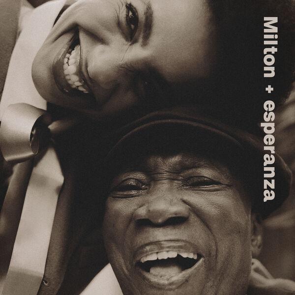 Black/white photo of old laughing man with a hat and younger smiling woman playfully resting her head on his