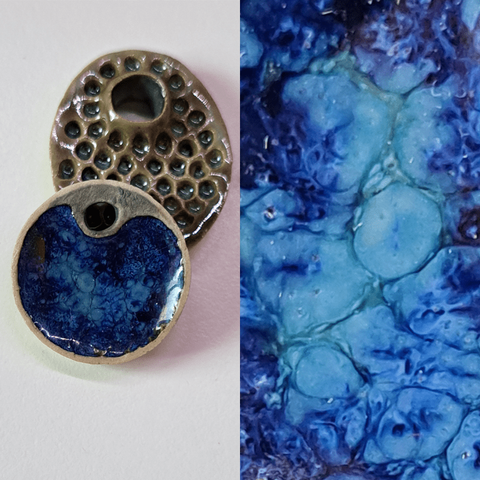 Two stoneware clay pendants, one leaning on the other which is mostly just there to hold up the former. In that one is a swirl of darker and lighter blur colours - the result of glazes mixing, floating together and creating marbled patterns.