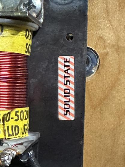 Closeup of a sticker saying SOLID STATE, planted on a flipper mechanism's base plate. The sticker is white with orange stripes.