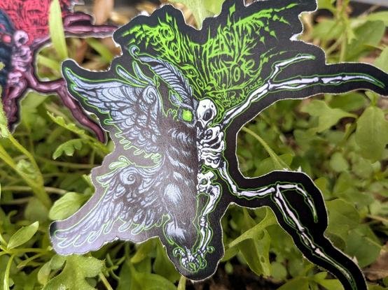 Close up on green mothman sticker with white bones, showing the semigloss texture sheen