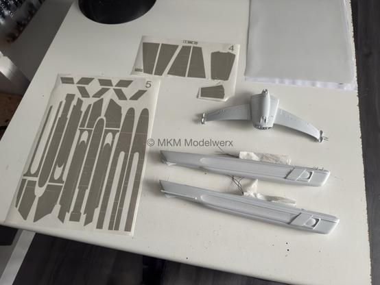 Model parts and sheets of vinyl paint masks on a white table.