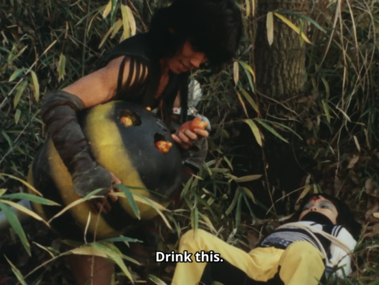 Amazon holding a giant severed bee abdomen, taking out some guts, and telling a mind controlled Masahiko to drink them to cure the mind control.