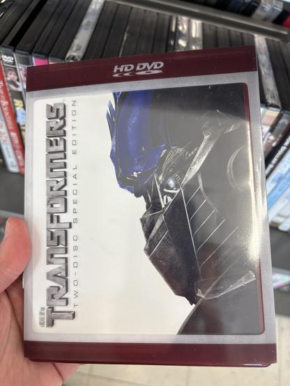 A copy of Transformers 2007 on HD DVD, held up in front of a shelf of random DVDs.