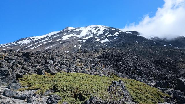 A tumbled lava field of black rock leading to the mountain's upper slopes still holding onto patchy snow.