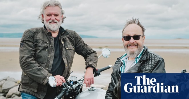 the two hairy bikers posing in leather jackets on motorbikes on a beach.