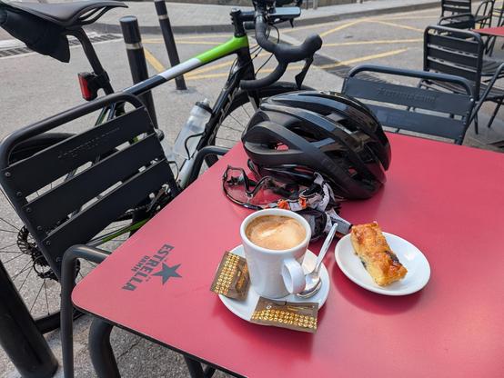 table with coffee and cake, bicycle helmet and gloves. bicycle leaning against the table.