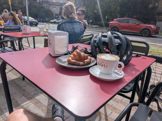 Coffee, croissant, and bicycle helmet on table near road in Barcelona