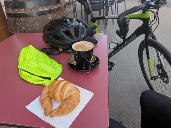 coffee table with coffee, croissant, bike helmet, and bicycle leaning against it