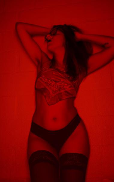 Foto minha em preto e vermelho. Em pé, com as mãos no cebelo, cabeça virada para o lado, de óculos de grau e batom preto. Vestindo meia 7/8 calcinha e top de lenço.