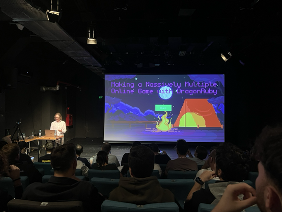 Julian Cheal standing in front of his opening pixelart style slide about writing massively multiple open games with ruby