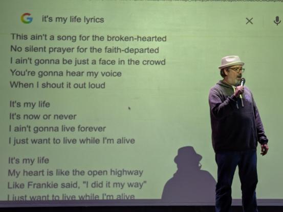Charles Nutter with a mic and the "It's my life" lyrics in the background