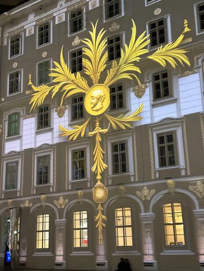Leafy gold emblem projected onto the side of a 5 story building that formed one side of a courtyard 