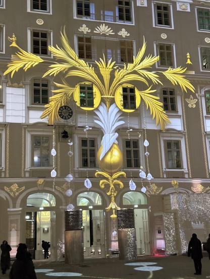 Leafy gold cat mask projected onto the side of a 5 story building that formed one side of a courtyard 