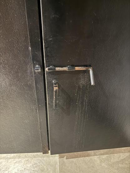 Large slide barrel lock on the inside of a bathroom stall door. The partition and the lock are made of metal.