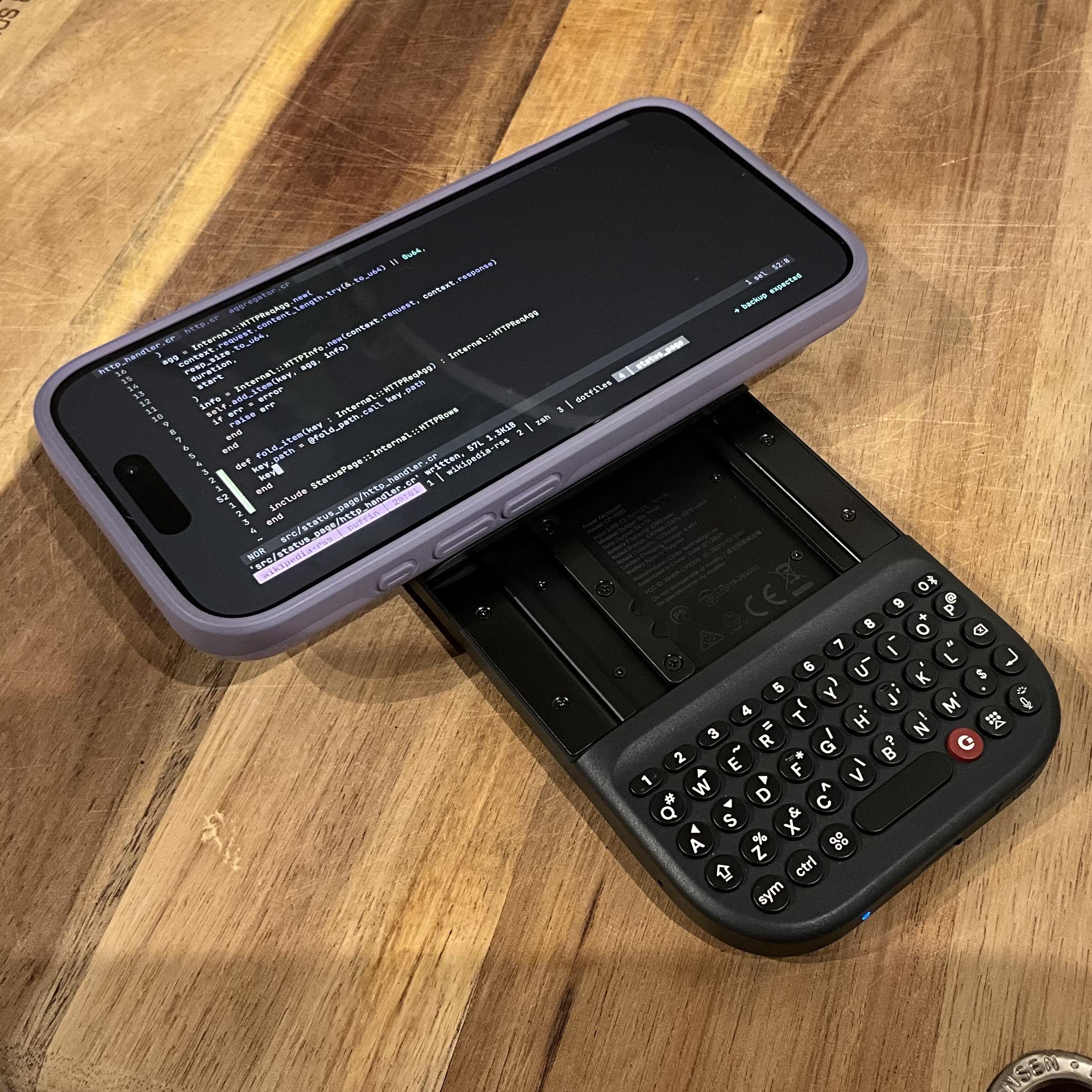 Clicks power keyboard attached to iPhone 15 pro in purple case on wooden chopping board

iPhone has blink (ssh client) open with tmux and helix with some crystal code