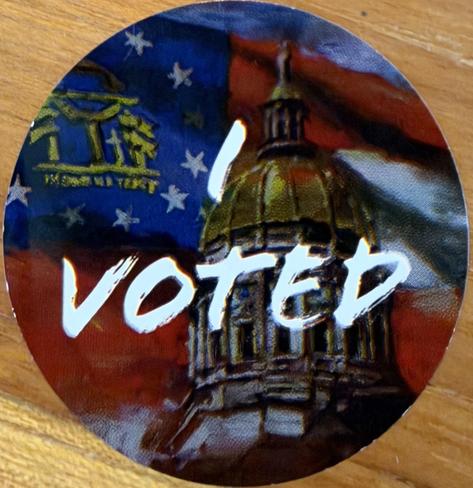 Round sticker with Georgia’s Capitol Dome (Gold Dome) and the Georgia state flag in the background. “I Voted” in what looks like oil paint in white.