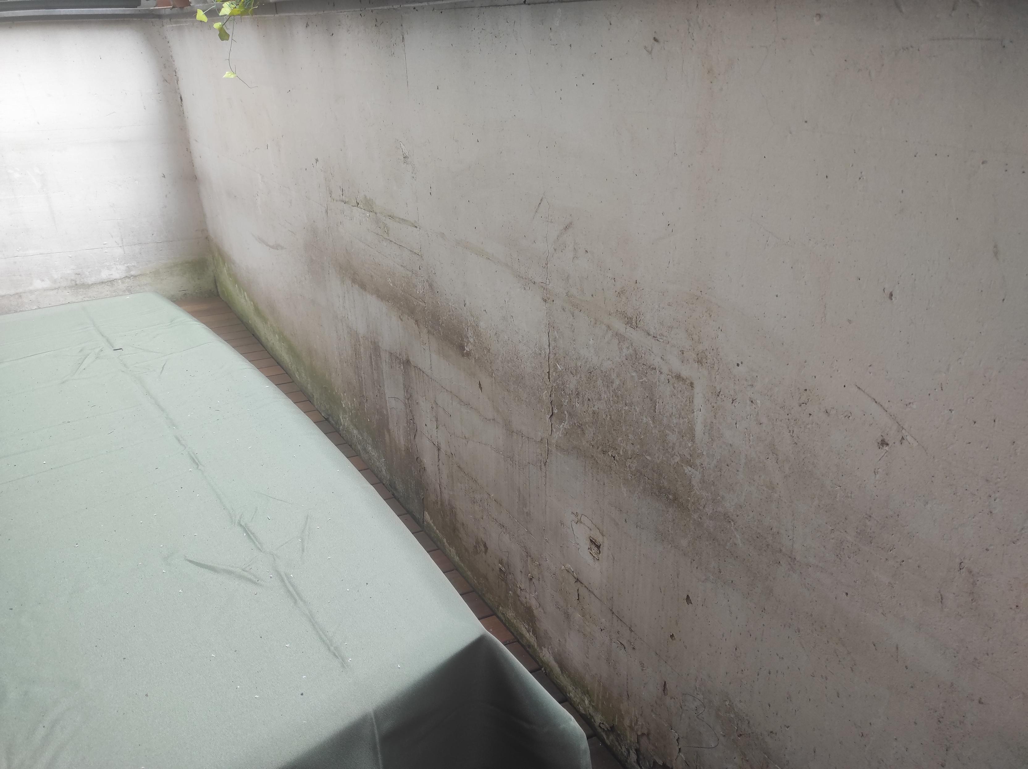 A dirty white wall. A covered table is visible on the left and there is wooden decking at the base.