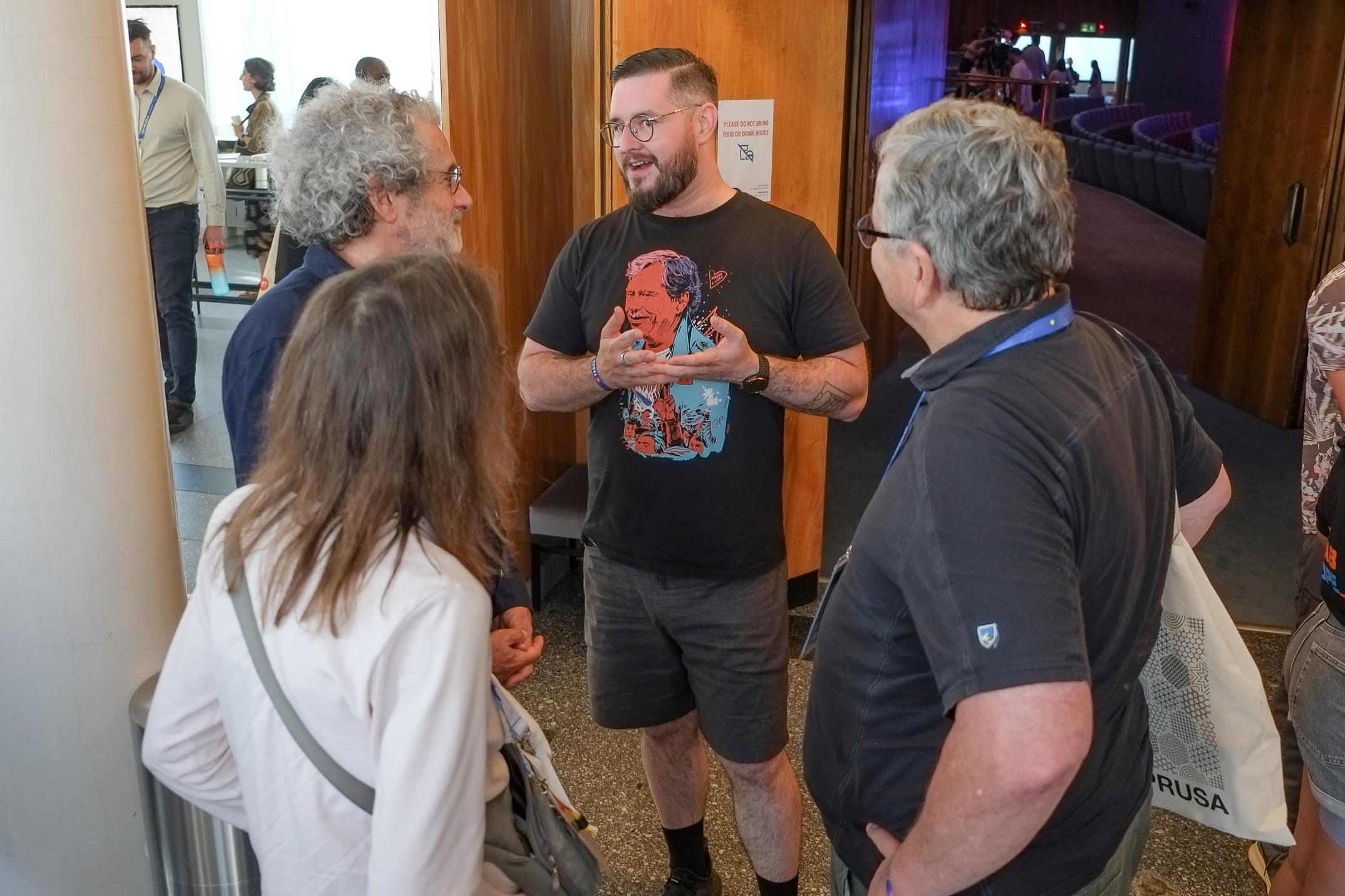 Photo of a man talking to two men and a woman with her back to the camera. FAB25 international fab lab annual conference, Brno, Czechia, 4 July 2025. Photo Cindy Kohtala