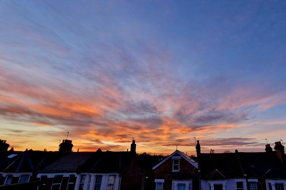 Sunset over a row of terraced House in North London, seen from the second floor of our house. The sky is painted in hues of yellow, orange, blue, pink and purple