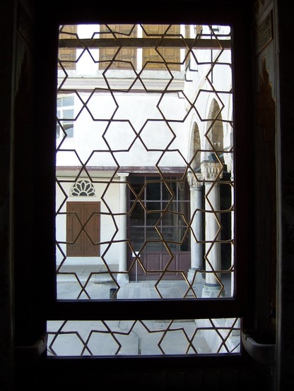 View from inside a house in Istanbul into a courtyard with columns on the right hand side. The window is patterned with hexagons and six pointed stars