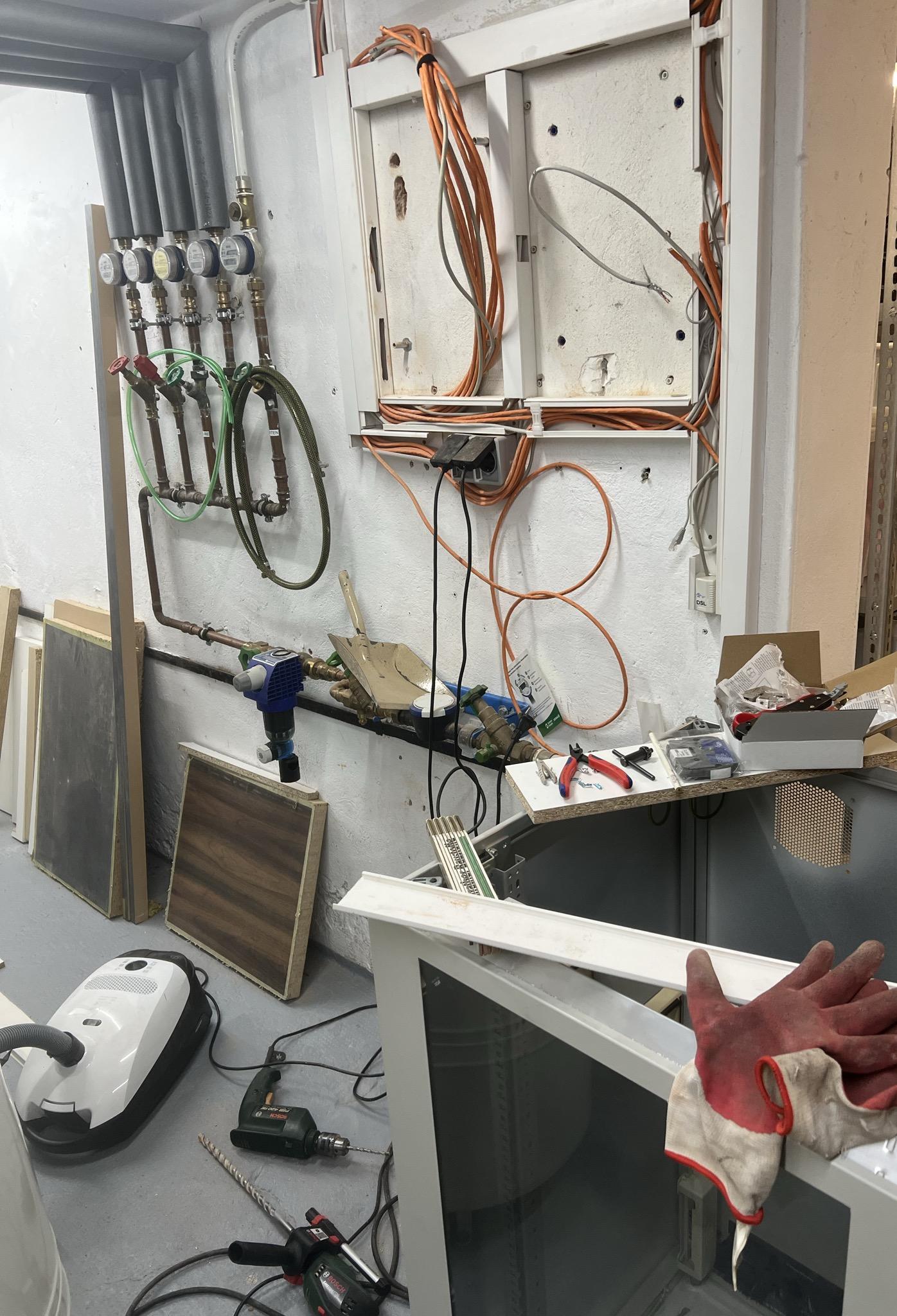 Keller, Haufen Netzwerkkabel, zwei Bohrmaschinen auf dem Boden, Staubsauger. Im Vordergrund ein völlig überdimensionierter 19 Zoll Schrank, für den nun Löcher durch die Wand gebohrt werden.