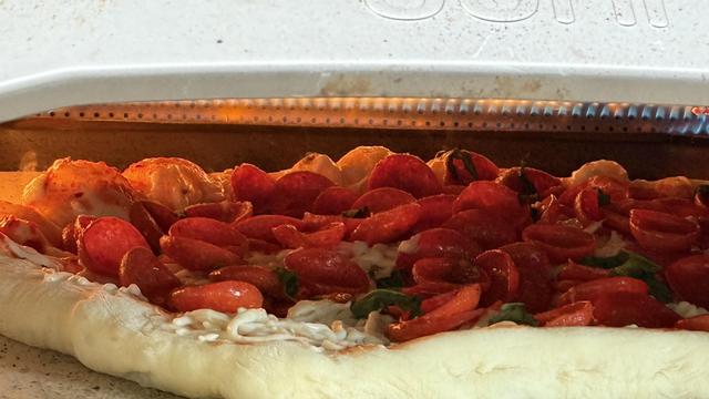 A cooking pizza with a little too much curling pepperoni.