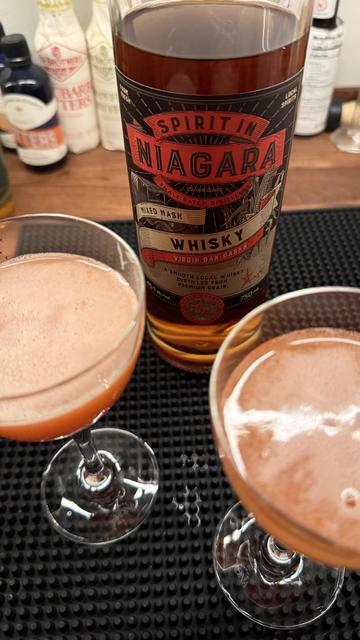 The mentioned whisky next to two glasses of Paper Plane cocktails.