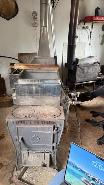Maple sap evaporator, steaming. Laptop in foreground. Finishing stove in background. Lazy lab number two snoozing next to the fires.