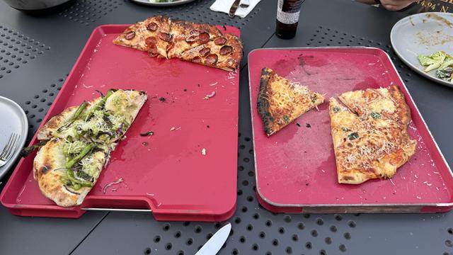 A table with red cutting boards; 3 kinds of pizza, partly consumed.
