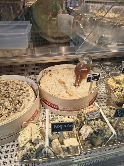 Two large wheels of gorgonzola with their tops cut off. One has an open bottle of cognac in it and the other is mixed through with fresh bits of black truffle. 
They are surrounded by smaller metal baskets of broken up stilton and Roquefort.