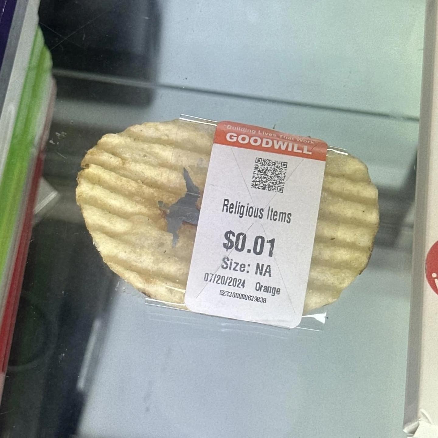 goodwill price tag on a slightly hollowed out piece of a potato crisp
the tag says "Religious Items; $0.01; Size: NA; 07/20/2024 Orange"