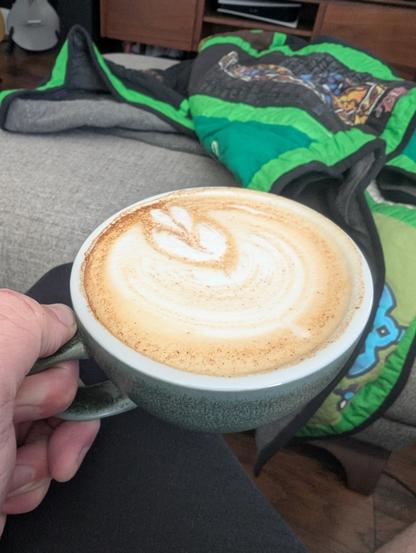Cafe latte with mediocre latte art and specks of cinnamon on top.