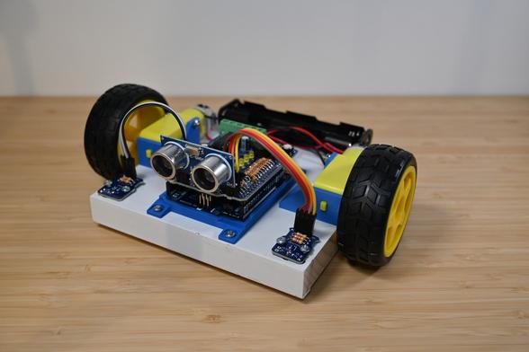 A simple classroom robot made using an Arduino UNO and an attached ARPS-2 shield holding an ultrasonic SONAR distance sensor module. The Arduino, both of ARPS-2' optical floor sensors, two inexpensive yellow plastic gear motors with attached wheels, and a four-AA battery holder are all screwed onto a small slab of white-painted scrap wood.