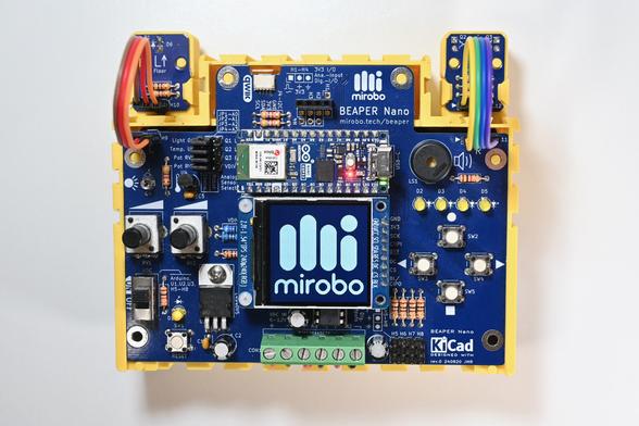 A top down view of a blue BEAPER Nano circuit board controlled by an Arduino Nano ESP32 microcontroller mounted above a graphical LCD showing the mirobo logo and word mark. The circuit is mounted in a yellow 3D-printed BEAPER Bot robot chassis, along with its two break-away optical floor sensor modules (top - connected by colourful extension cables).