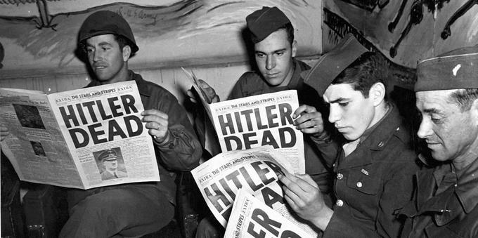 A bunch of soldiers reading newspapers that have a headline that says "Hitler Dead."