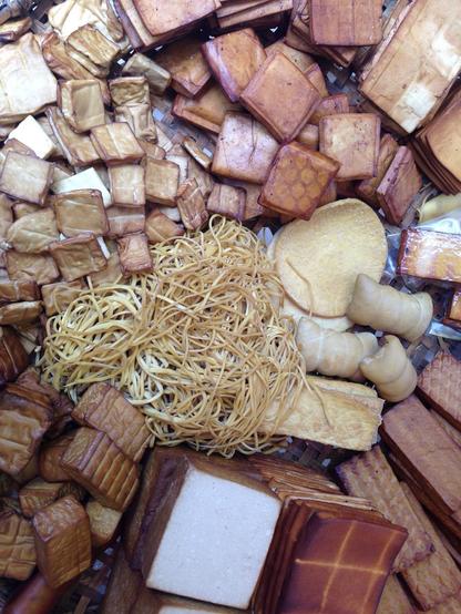 A variety of shapes and sizes of soy products, mainly in varying shades of brown and some white. Handmade and sold without any packaging.
