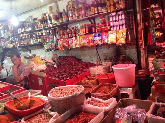 Indoor market stall, one man seated to the left, lots of red dried peppers of various kinds on offer.