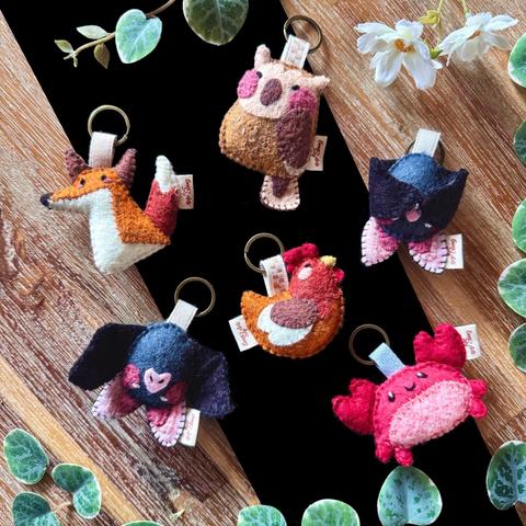 A collection of 6 keychains on the same type of background: a fox, an owl, two bats, a crab and a chicken.