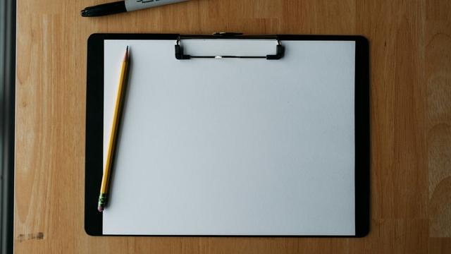 Ein Klemmbrett mit einem leeren Platt Papier und zwei Stiften